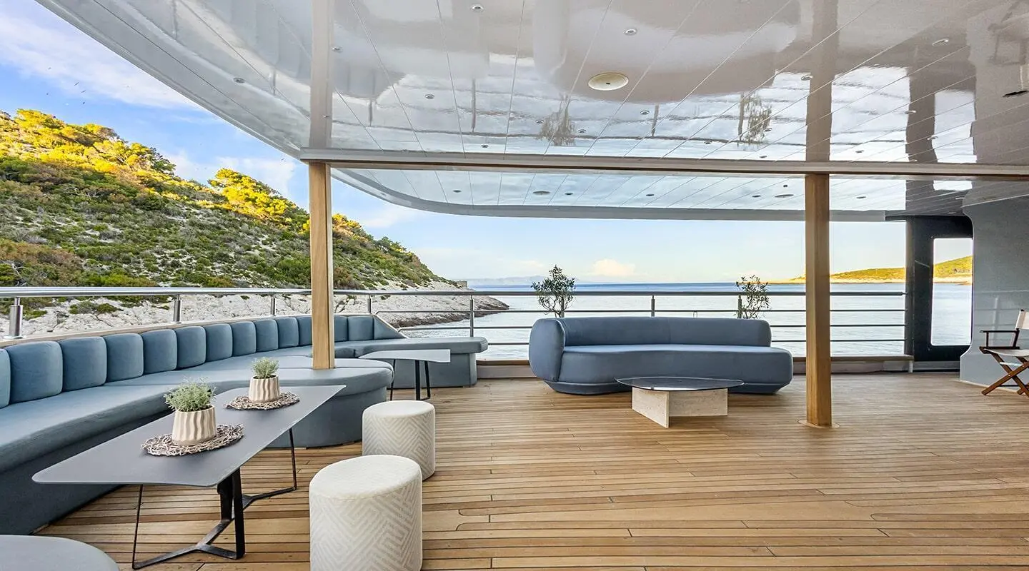 Bella yacht deck with cushioned seating, wooden floor, and sunlit railing