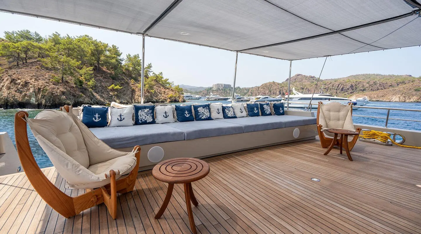Wide deck seating area on luxury yacht De Love with cushions and round wooden stools