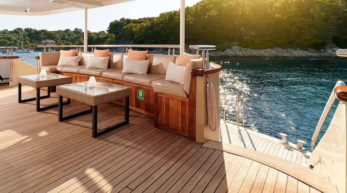 Sunlit deck with beige sofa and cushions; water and green trees in the background