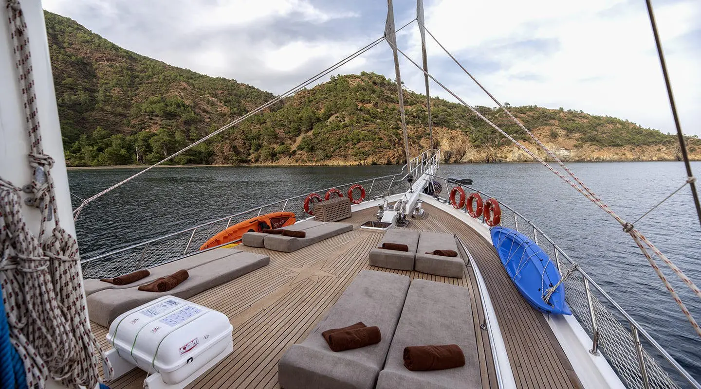 Kayhan 3 yacht deck view at sunset, sailboat beside rocky shoreline