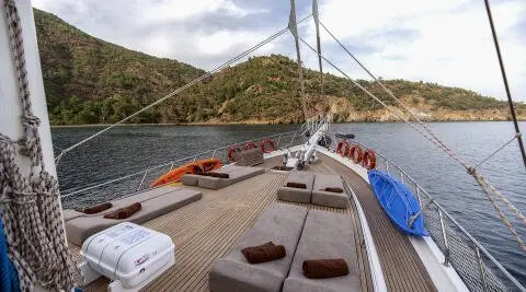 Kayhan 3 yacht deck view at sunset, sailboat beside rocky shoreline