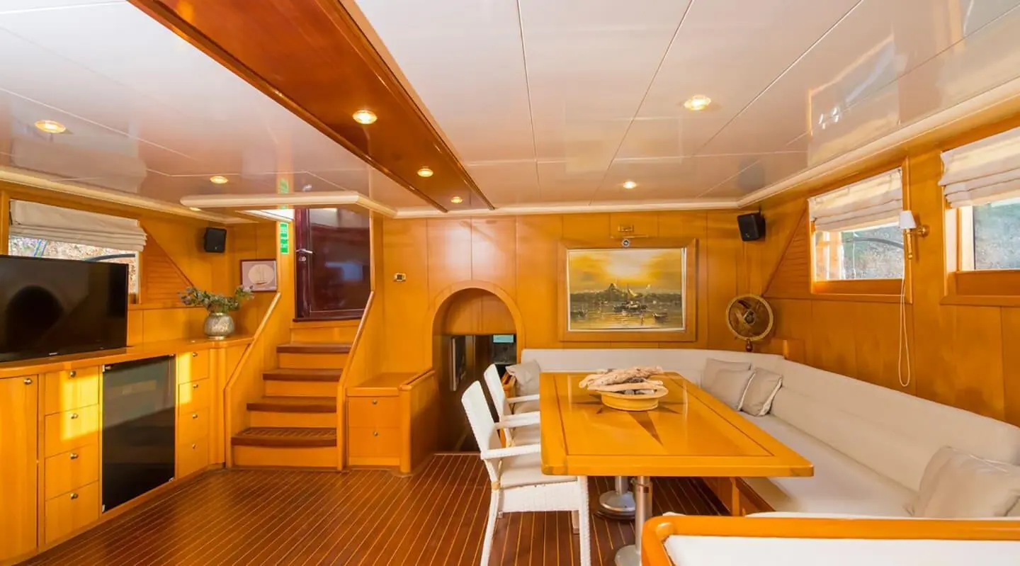 Cozy yacht interior with wooden panels, dining table, stairs, and porthole views
