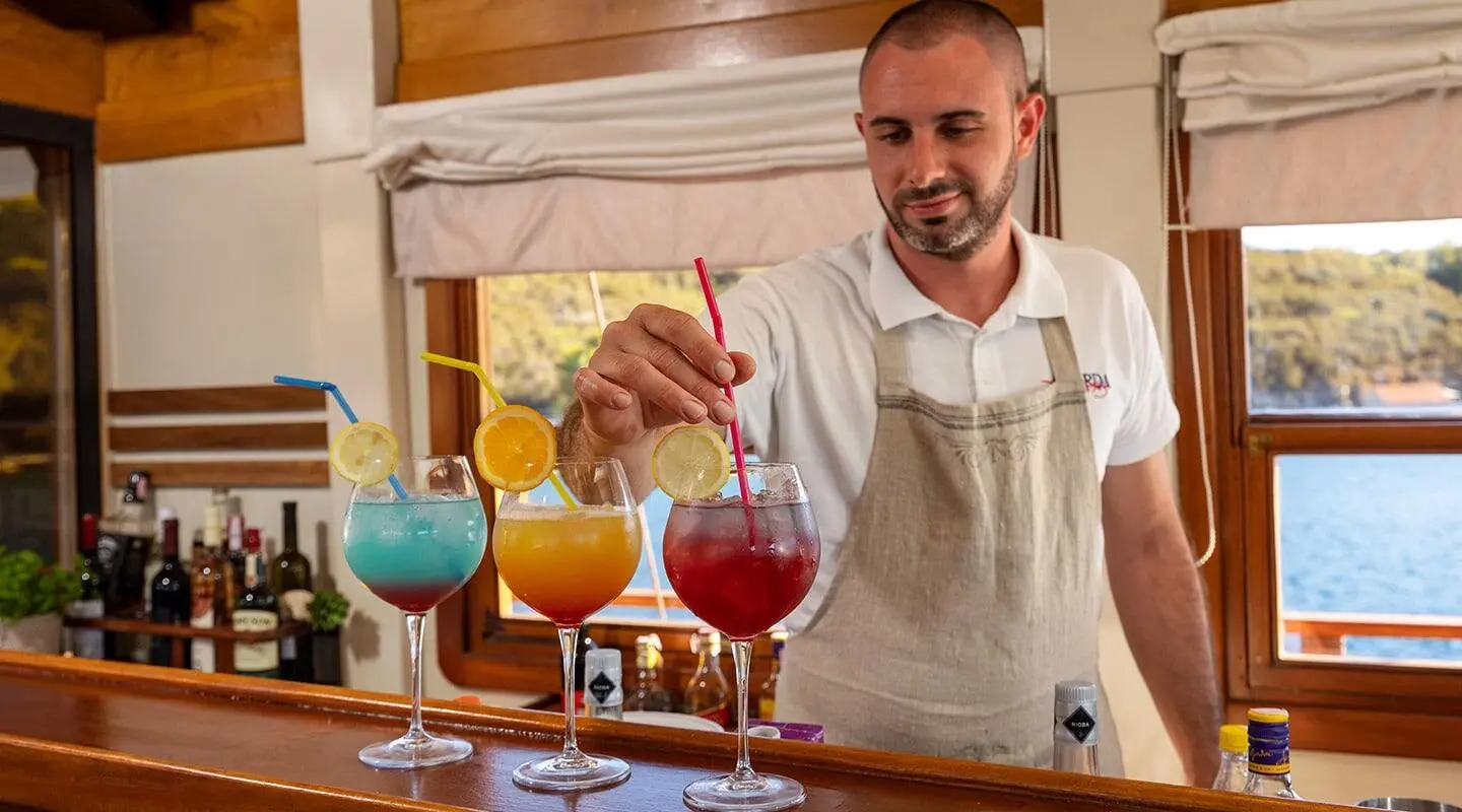 Yacht Aborda bar scene with bartender serving colorful cocktails at sunset