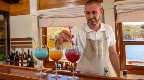 Yacht Aborda bar scene with bartender serving colorful cocktails at sunset