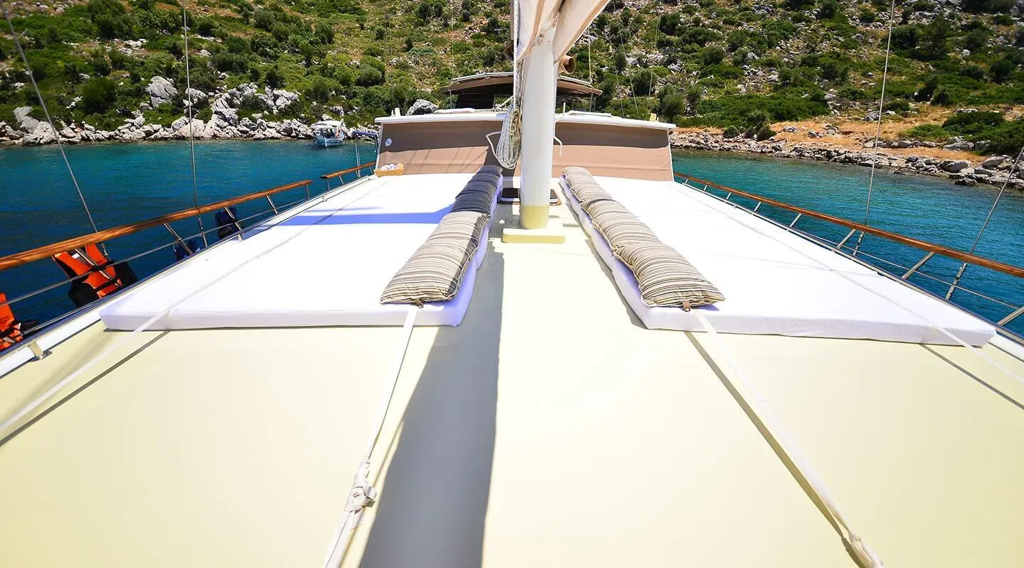 Sun deck view with mast and teak railings, rocky coastline in the background