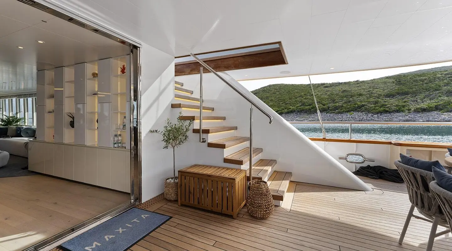 Maxita yacht aft deck with wooden stairs, railing, and wicker storage chest