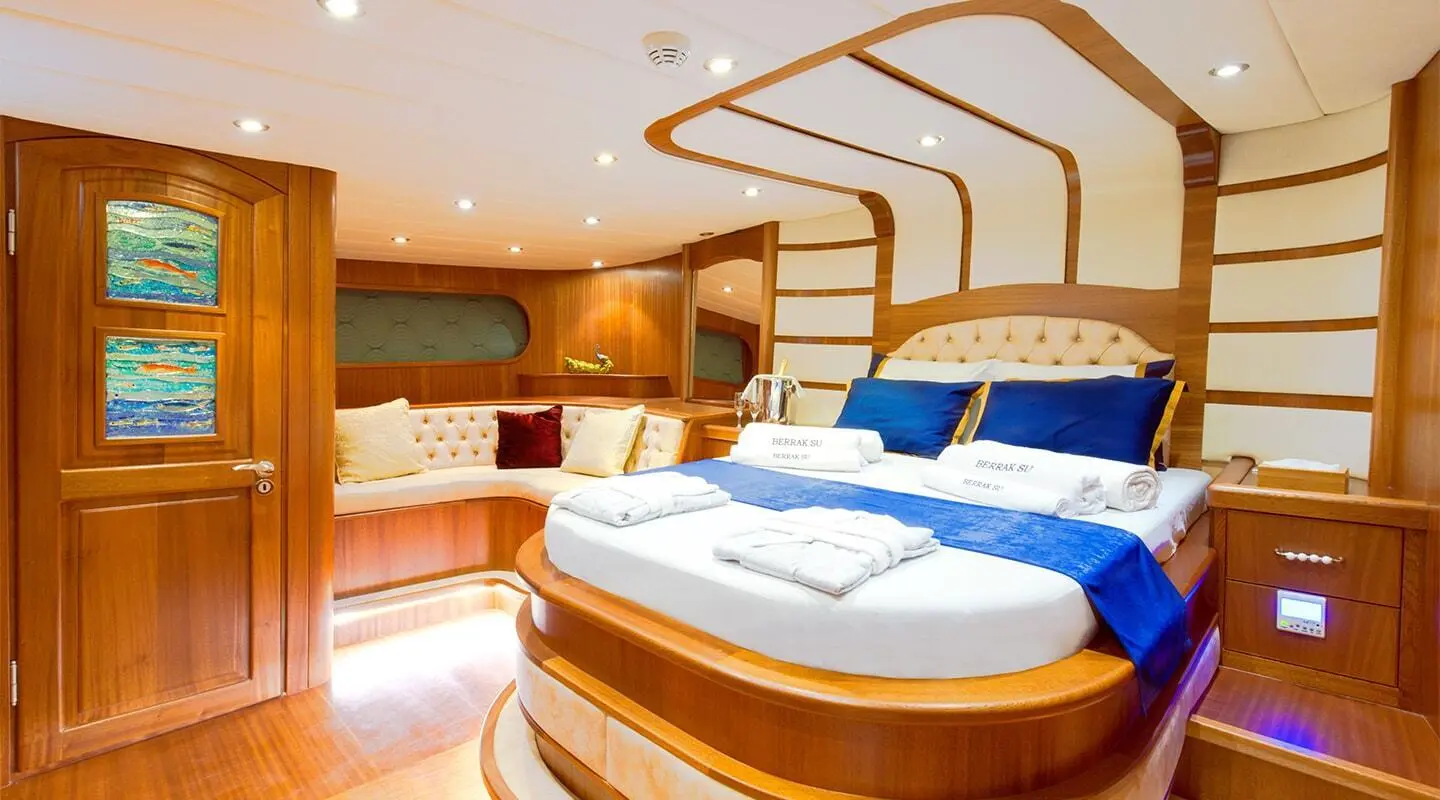 Berrak Su yacht interior with circular bed, warm wood tones and blue cushions