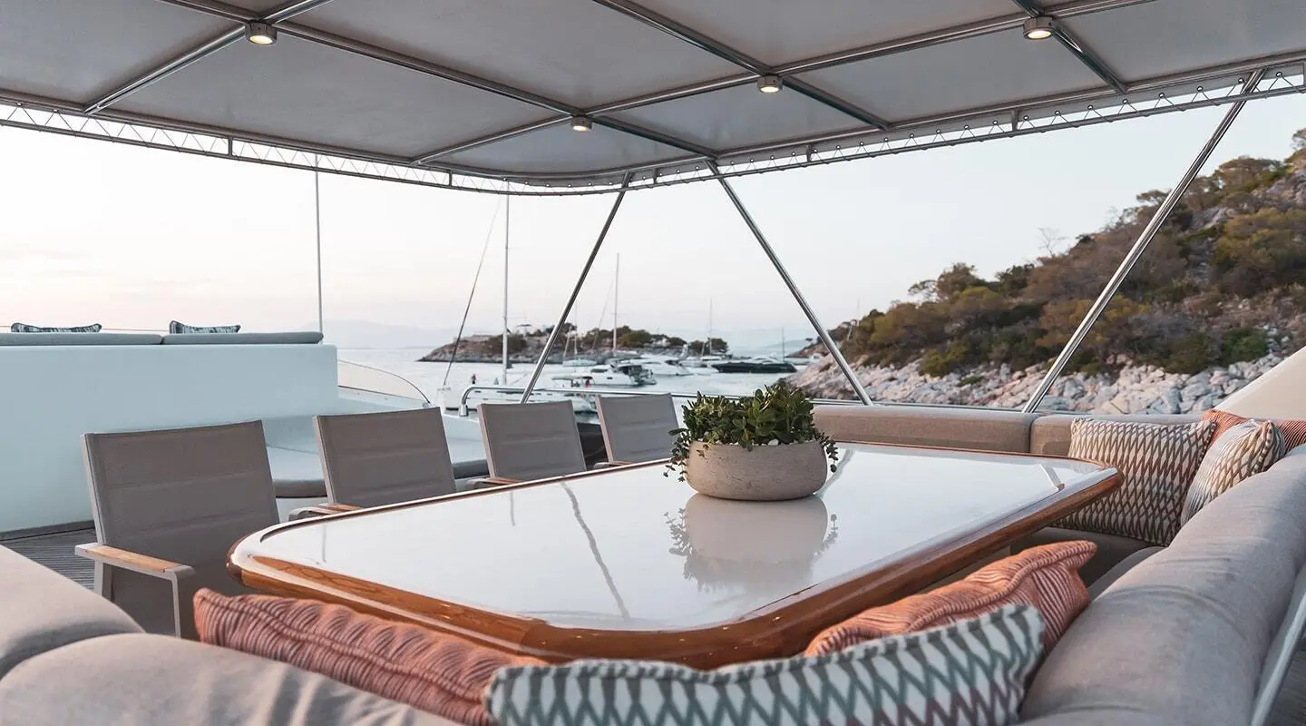 Aquila yacht exterior lounge with a glossy table and cushioned seating under a canopy