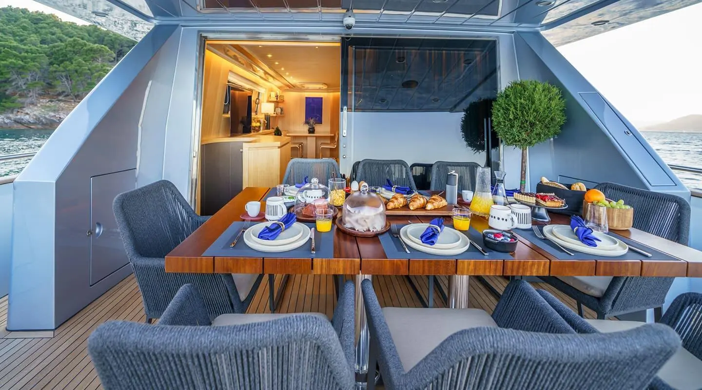 Wooden dining table set for breakfast with croissants on an outdoor yacht deck