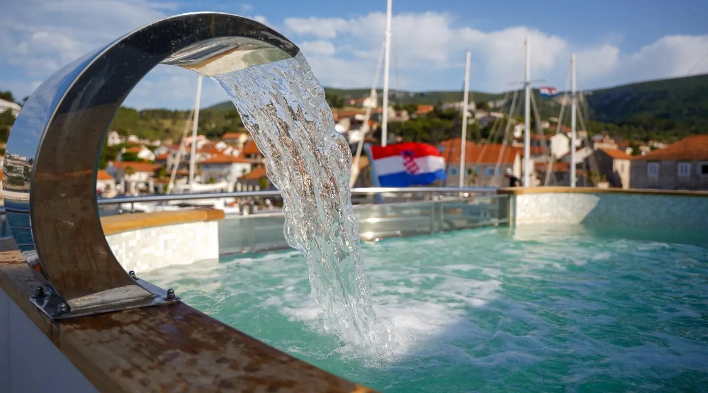 Yacht Freedom at sea with splash arc over pool area and deck chairs
