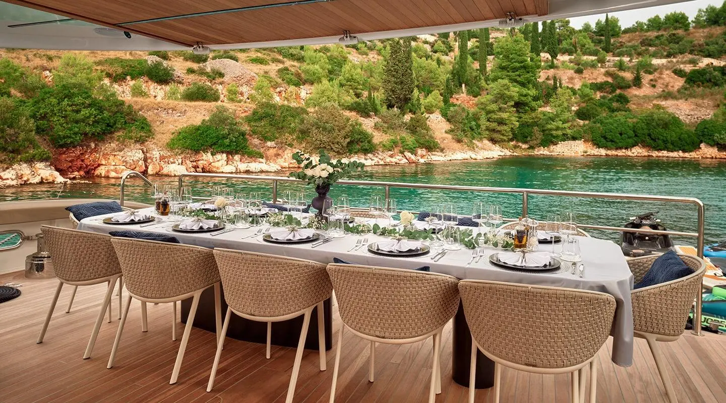 Yacht Anetta dining deck with chairs facing turquoise water and rocky shore