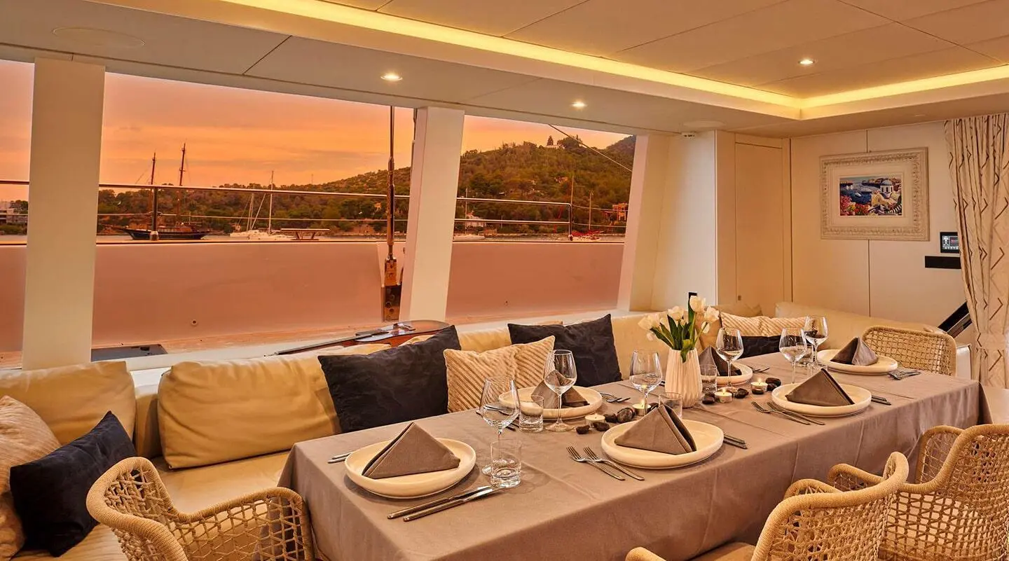 Gently lit yacht dining table set for sunset on deck with plates and glassware