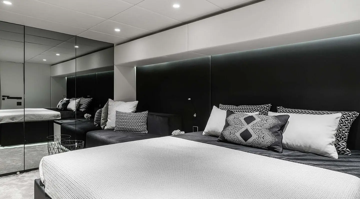 Interior of a yacht cabin with dark paneling, white bedding, and cushions