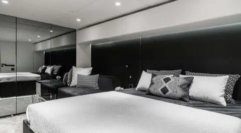 Interior of a yacht cabin with dark paneling, white bedding, and cushions