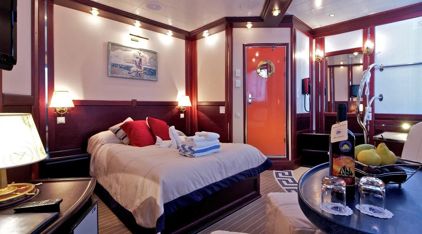 Luxurious yacht cabin with two beds, warm lighting, navy blue bedding and red accents