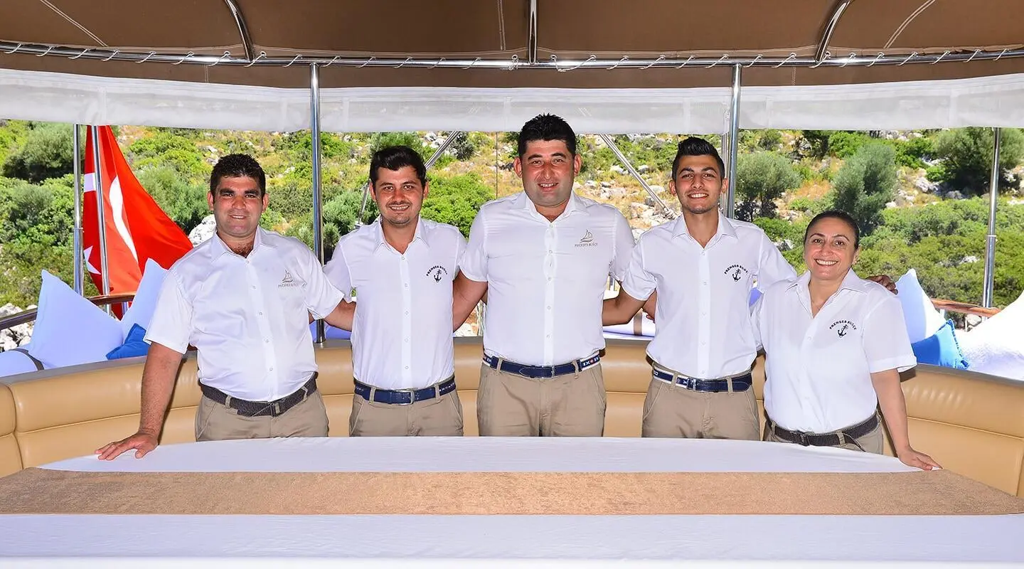 Prenses Bugce yacht crew standing on deck at sunset, luxury gulet sailboat
