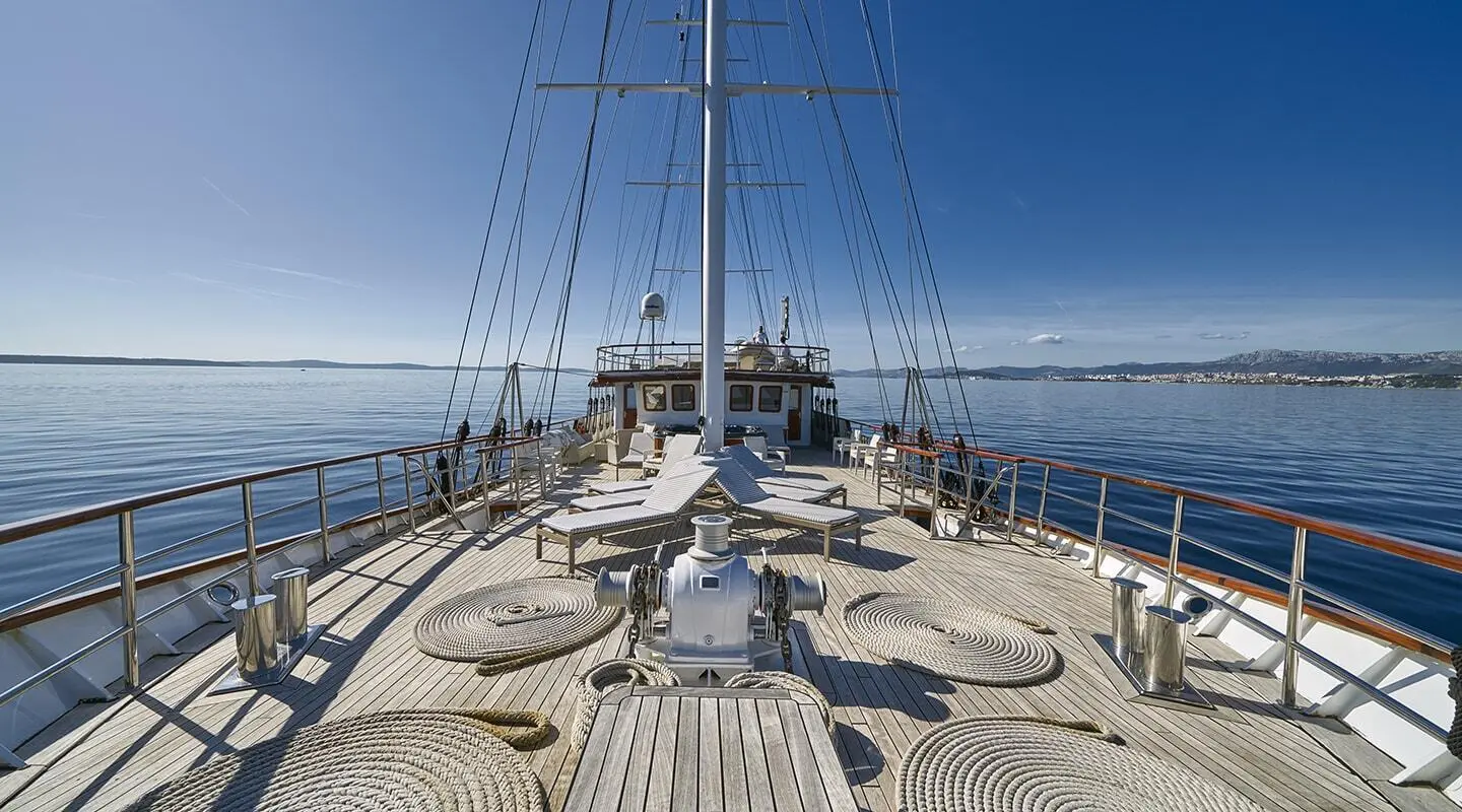 Sunlit deck of Amorena yacht, lines and railing with calm sea ahead