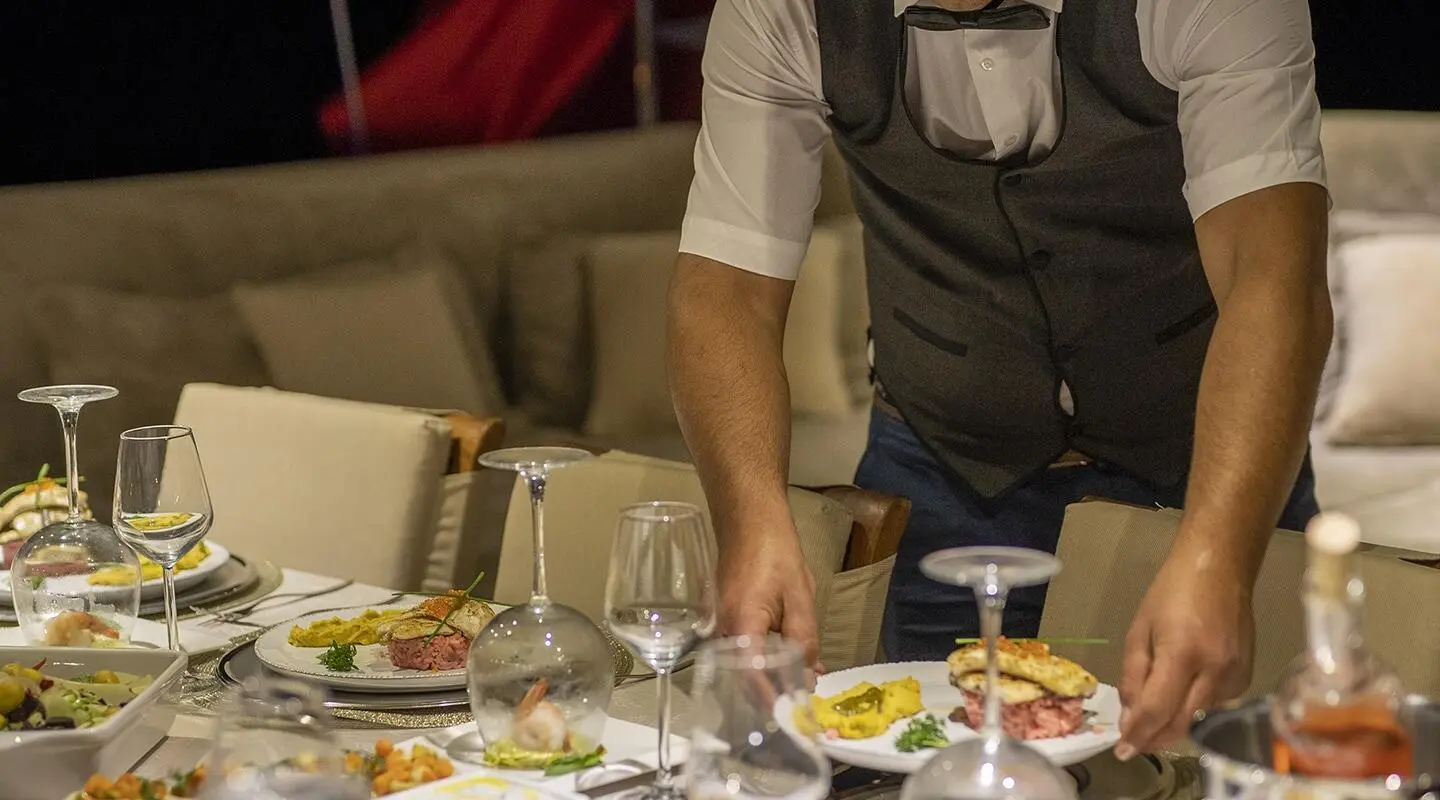 Arabella yacht dining scene onboard, waiter serving plates at table