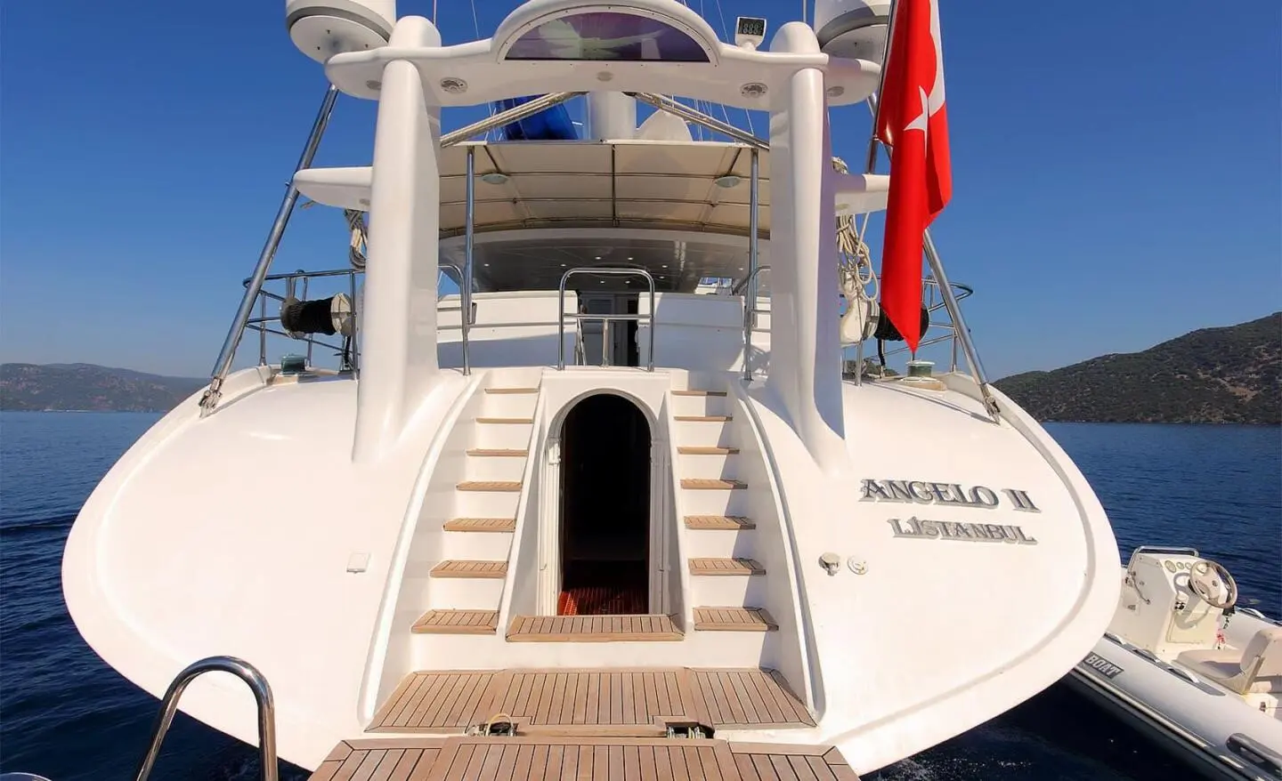 Angelo II yacht deck with stairs, railings, sun loungers, and red flag at sunset