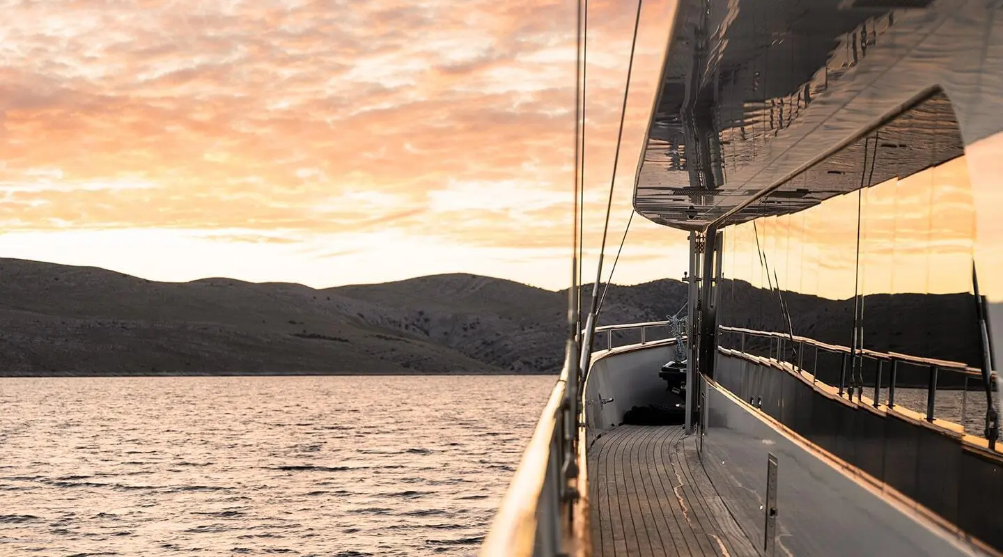 Yacht Maxita side deck at sunset, railing, deck fittings, calm water horizon