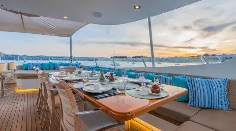 Serenity yacht dining area on deck at sunset with tables and chairs, ocean view