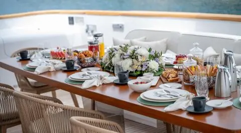 Pareaki II yacht table setting with plates, wine, and flowers on deck