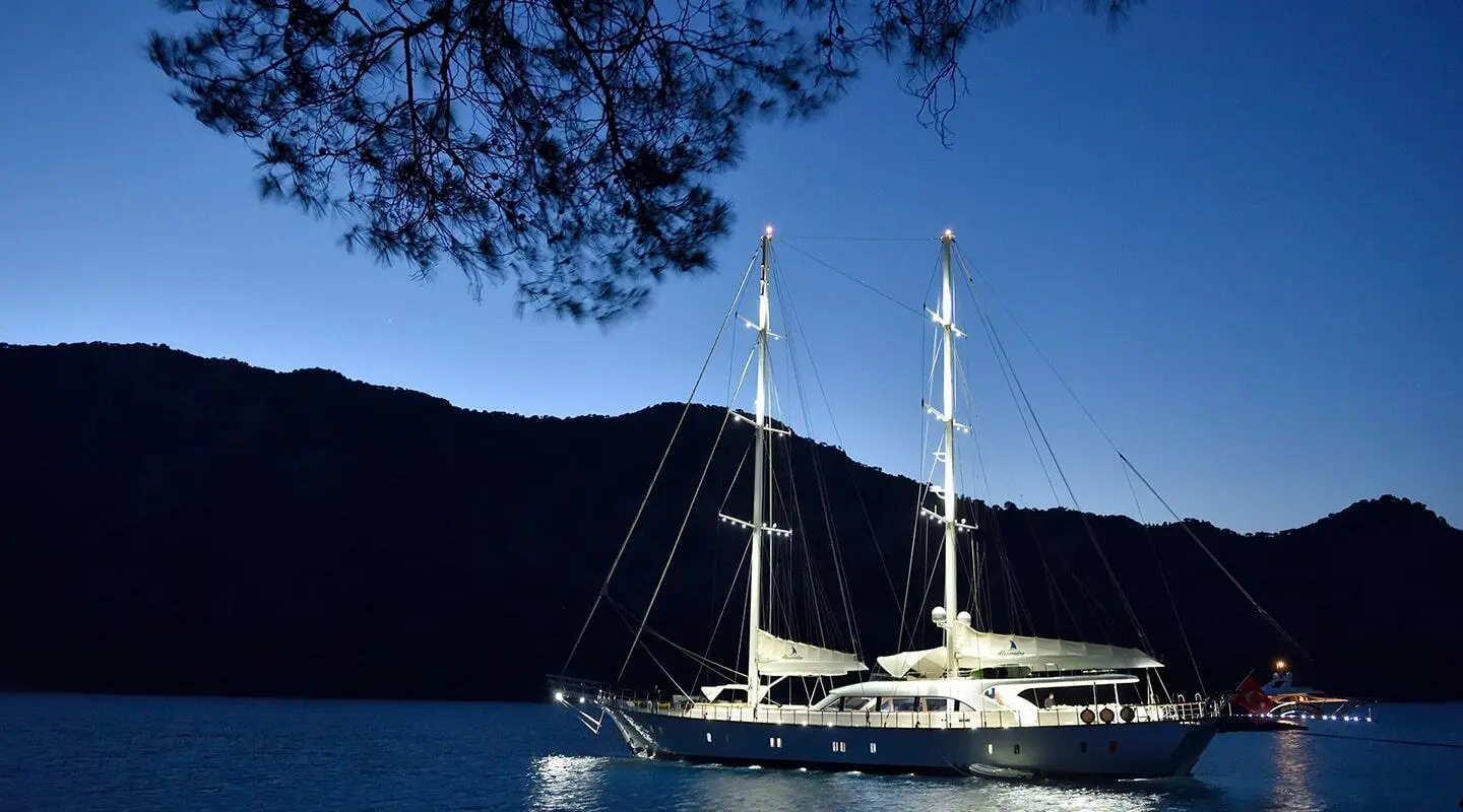 Alessandro I yacht anchored at sunset with calm blue water and hills