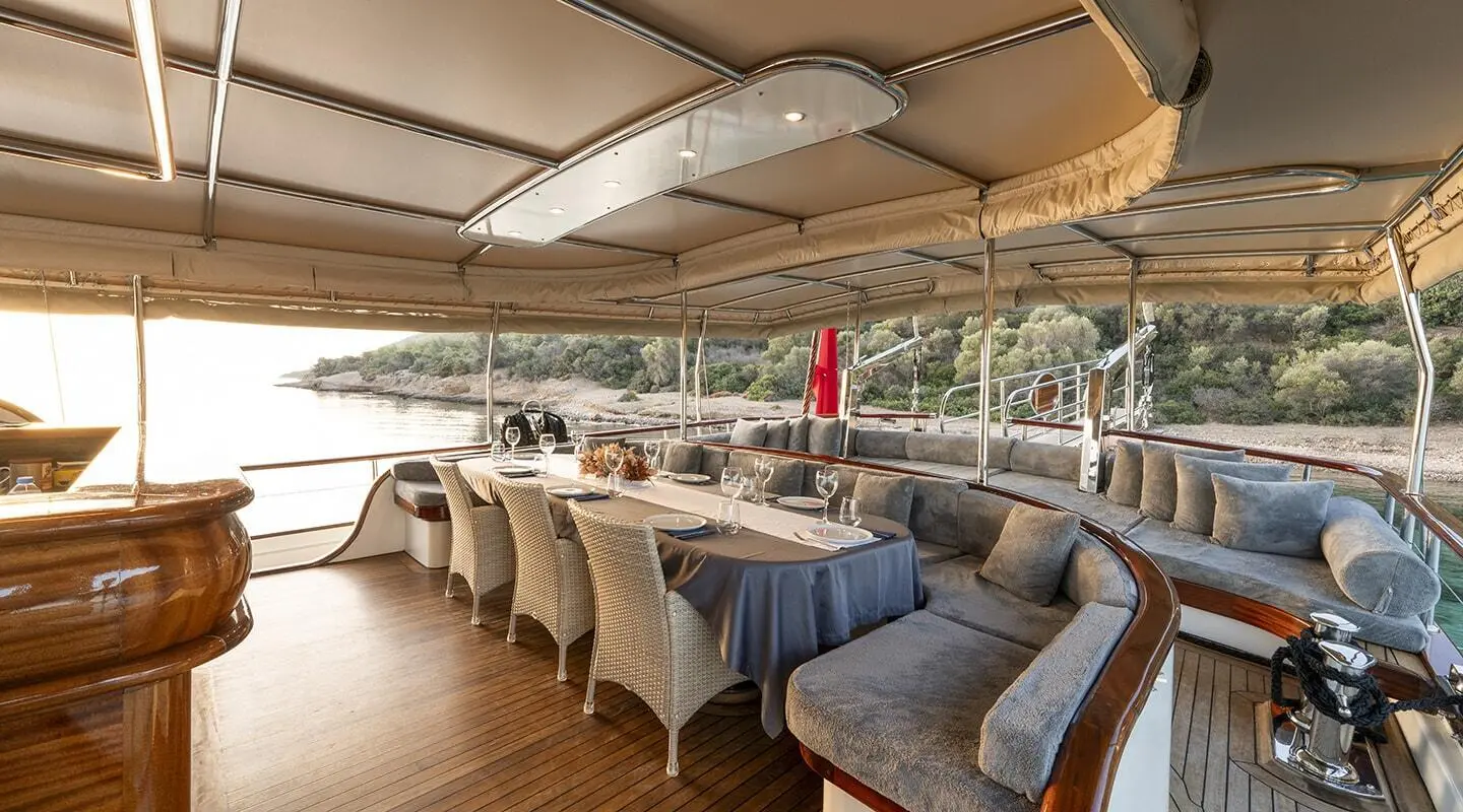 Dining table with chairs and a long sofa on the deck, sea and shoreline in the background