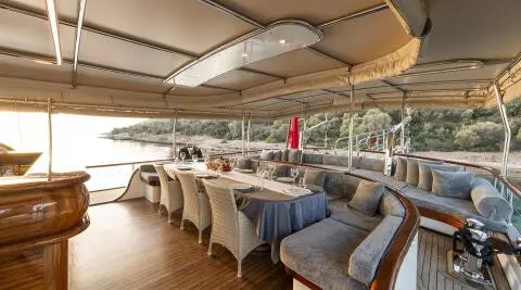 Dining table with chairs and a long sofa on the deck, sea and shoreline in the background