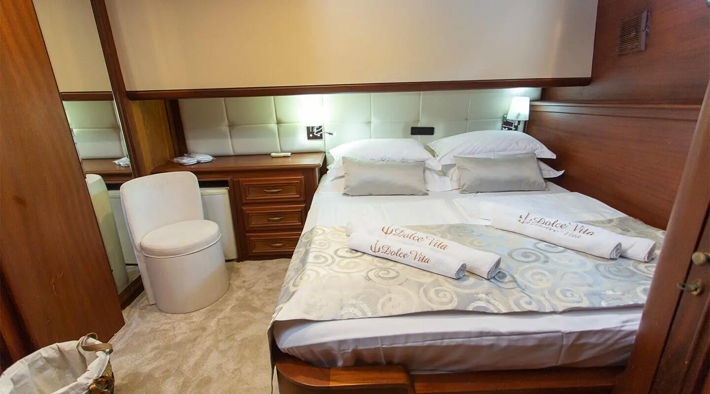 Interior of Dolce Vita yacht: large bed, pillows, wooden furniture, warm lighting