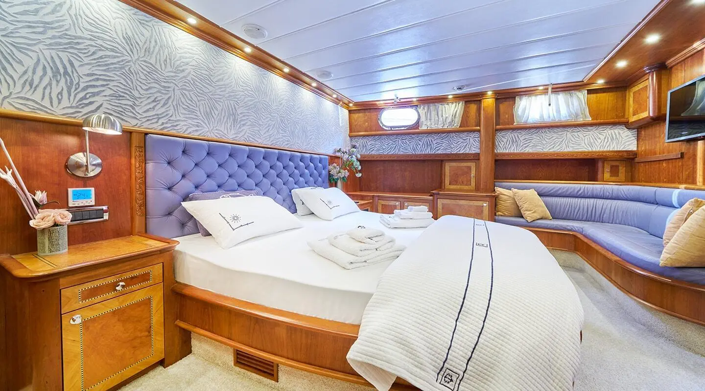 Luxurious yacht Lotus interior: large bed, wooden cabinets, blue upholstered seating
