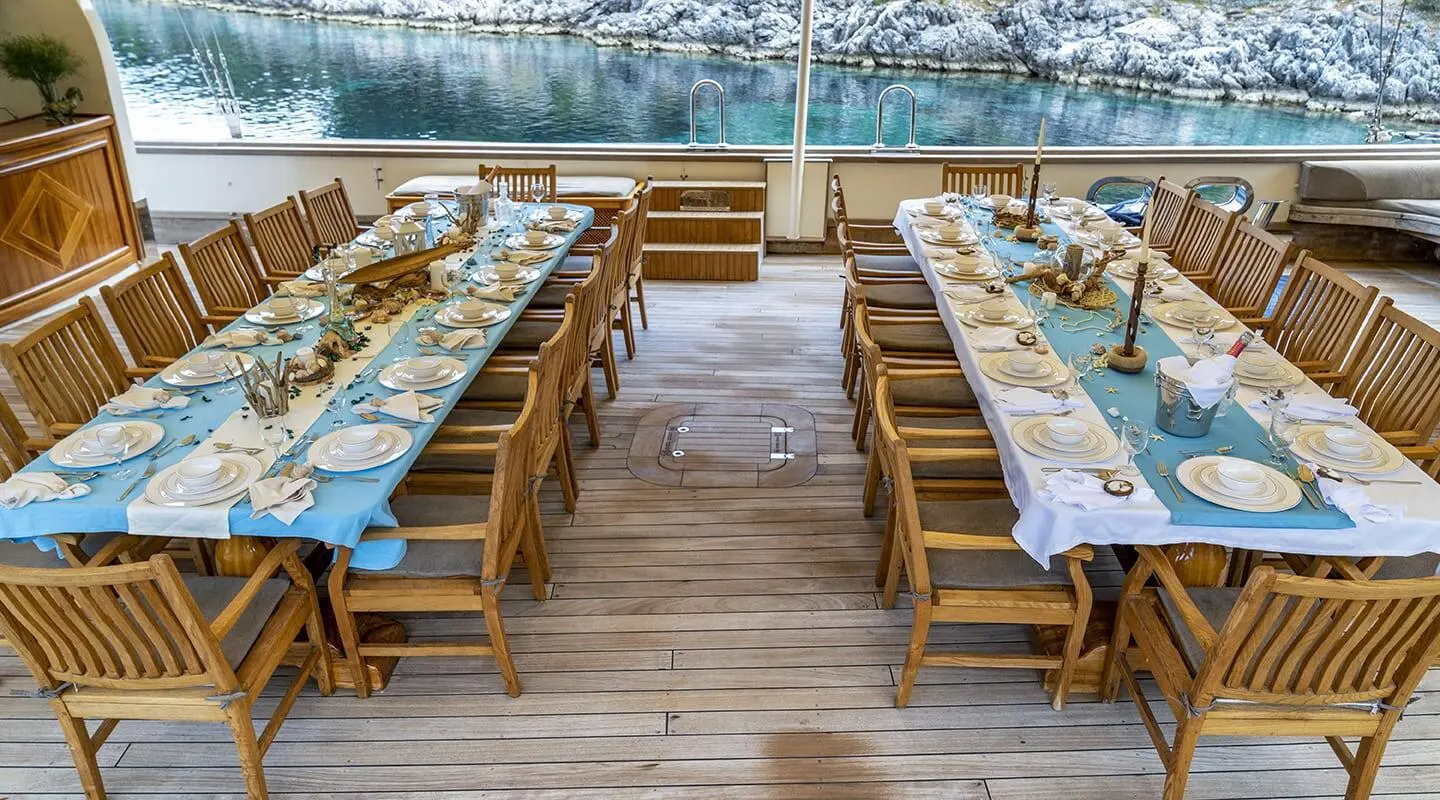 Tersane 8 yacht dining area on a wooden deck with long tables and blue tablecloths