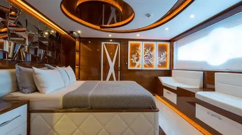 Interior view of a yacht cabin with a large bed, wooden accents, and ceiling skylight