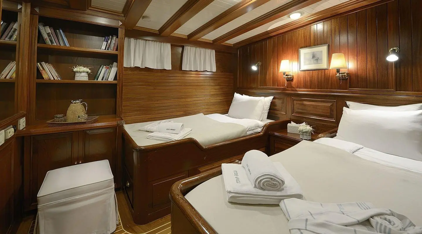 Twin cabin aboard Ecce Navigo: two beds, wooden panels, folded towels on table
