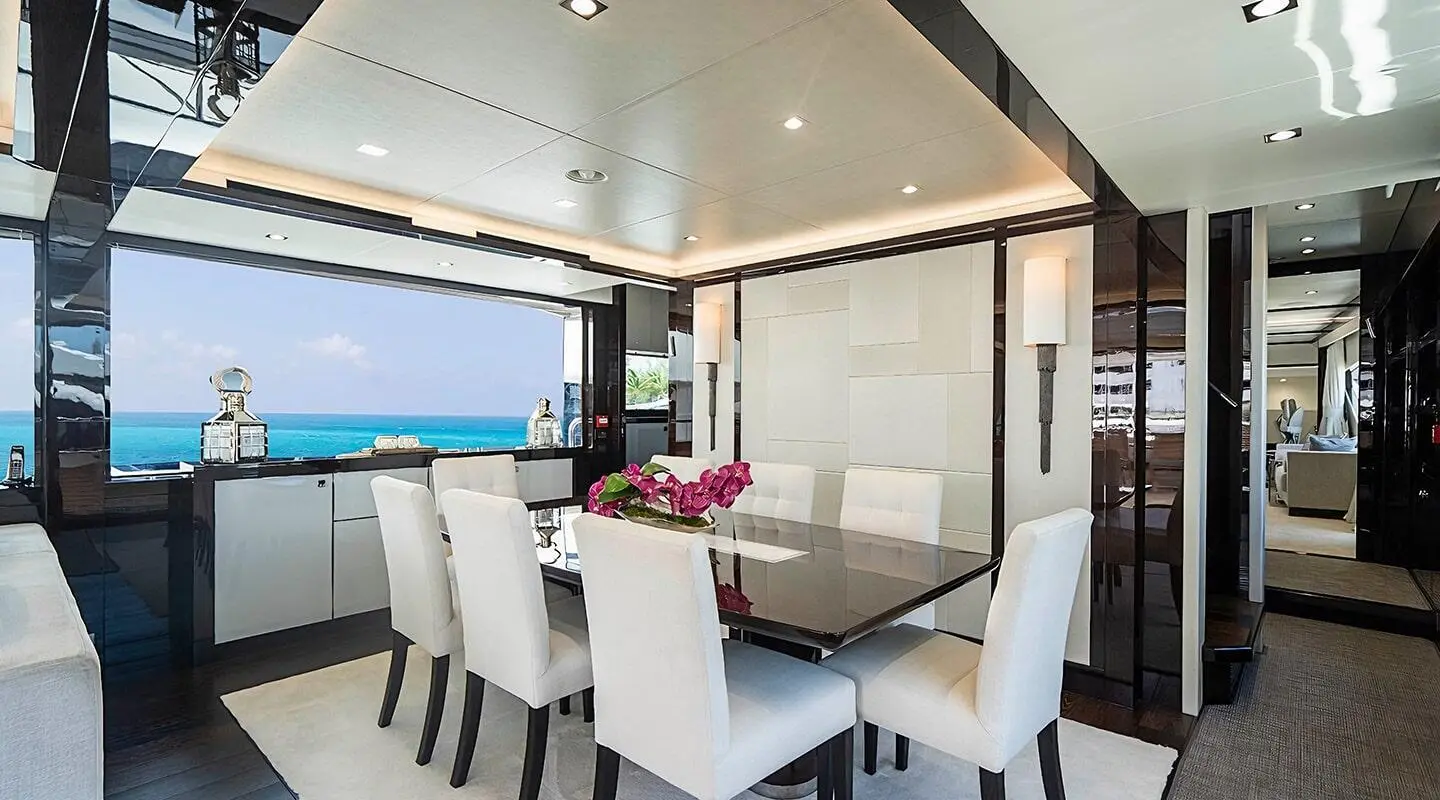 White dining chairs around a glass table inside with ocean view through large windows