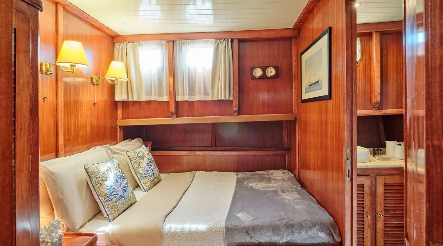 Cozy yacht cabin with wooden walls, bed, and window view at sunset