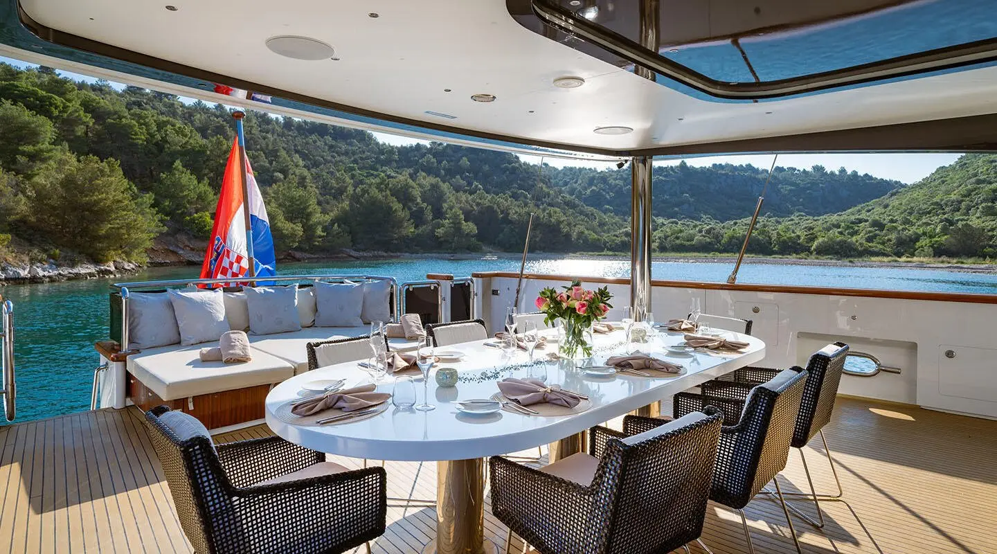 Navilux yacht aft deck with table set for guests, scenic sea and hills