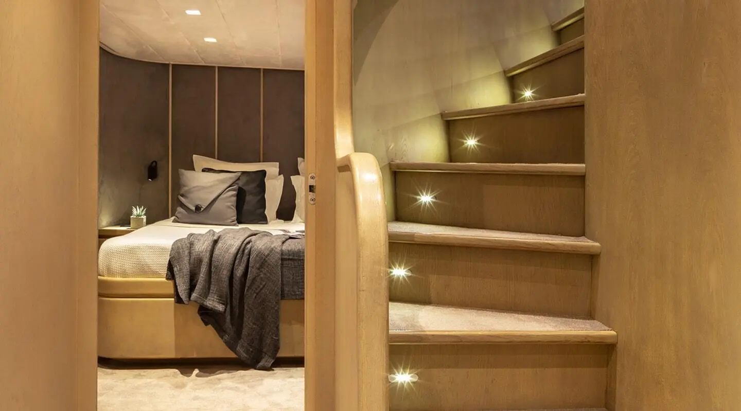 Interior view of a yacht with a wooden staircase and a bedroom in background