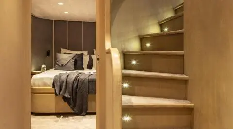 Interior view of a yacht with a wooden staircase and a bedroom in background