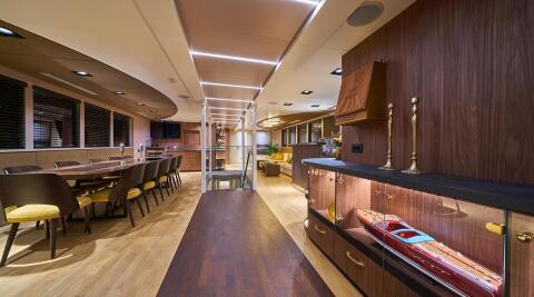 Luxurious interior of Rara Avis yacht: long dining table, modern wood panelling, and a glass display case with a model boat