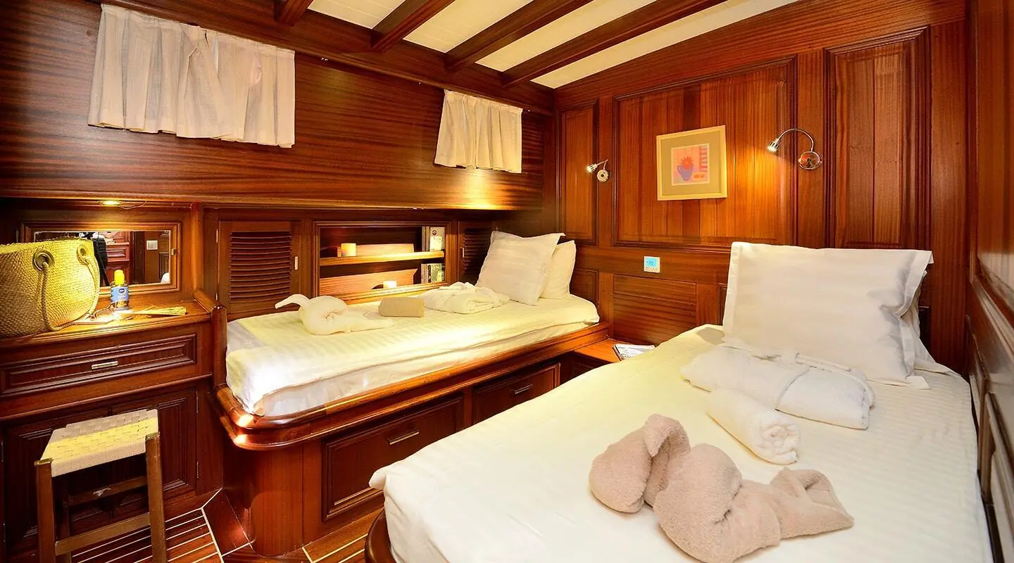 Interior of a yacht cabin with two beds, wooden walls, and folded towels on a bed