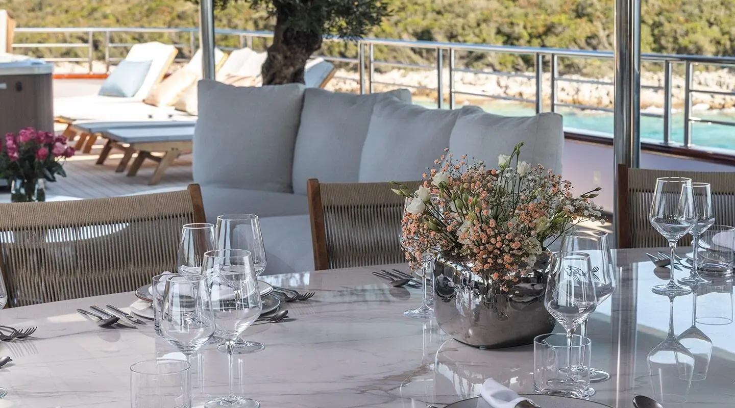 Table setup on a yacht deck with flowers, glassware, and plates under a shaded area