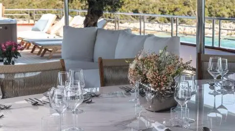 Table setup on a yacht deck with flowers, glassware, and plates under a shaded area