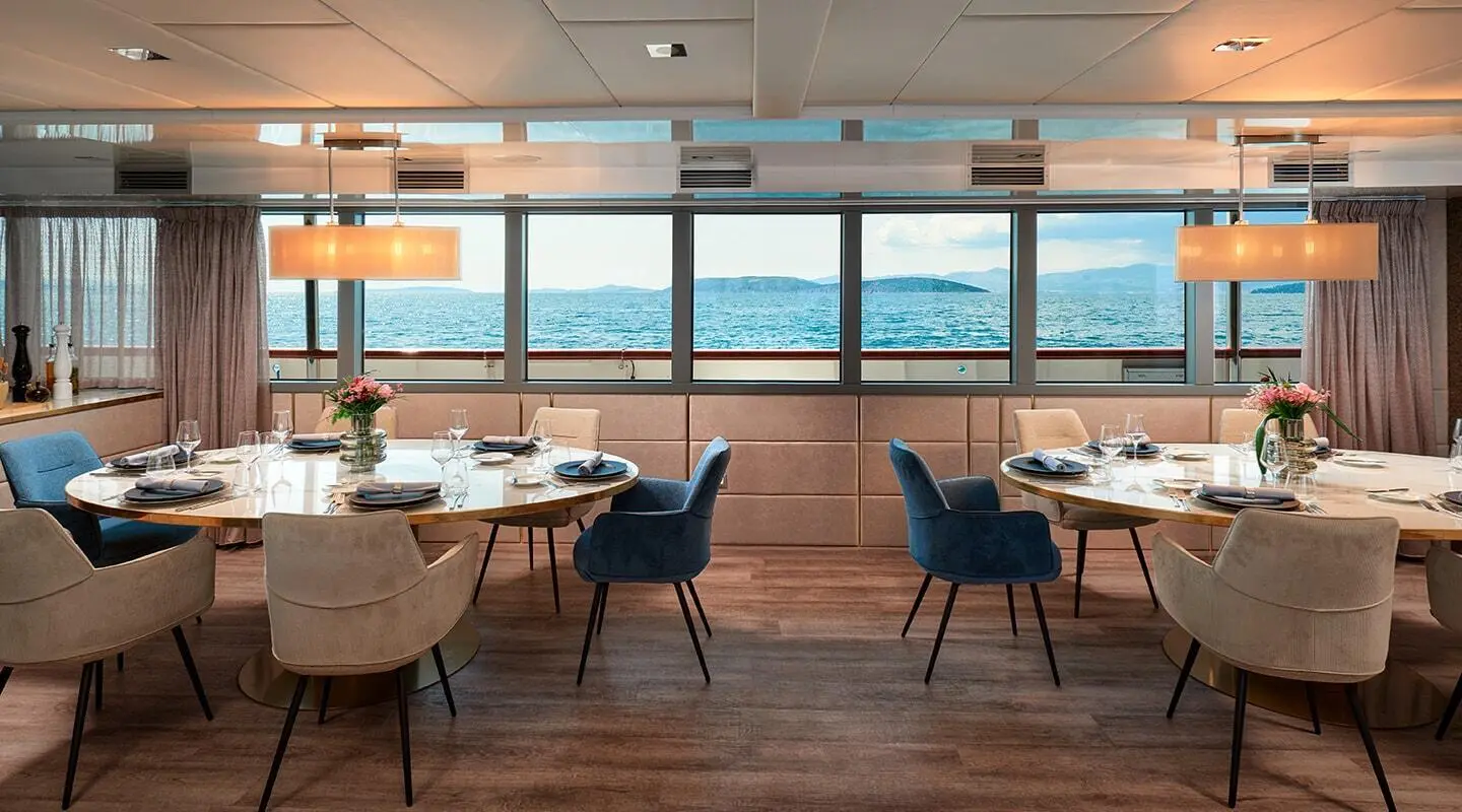 Interior of Ohana yacht salon with round tables and blue chairs by windows