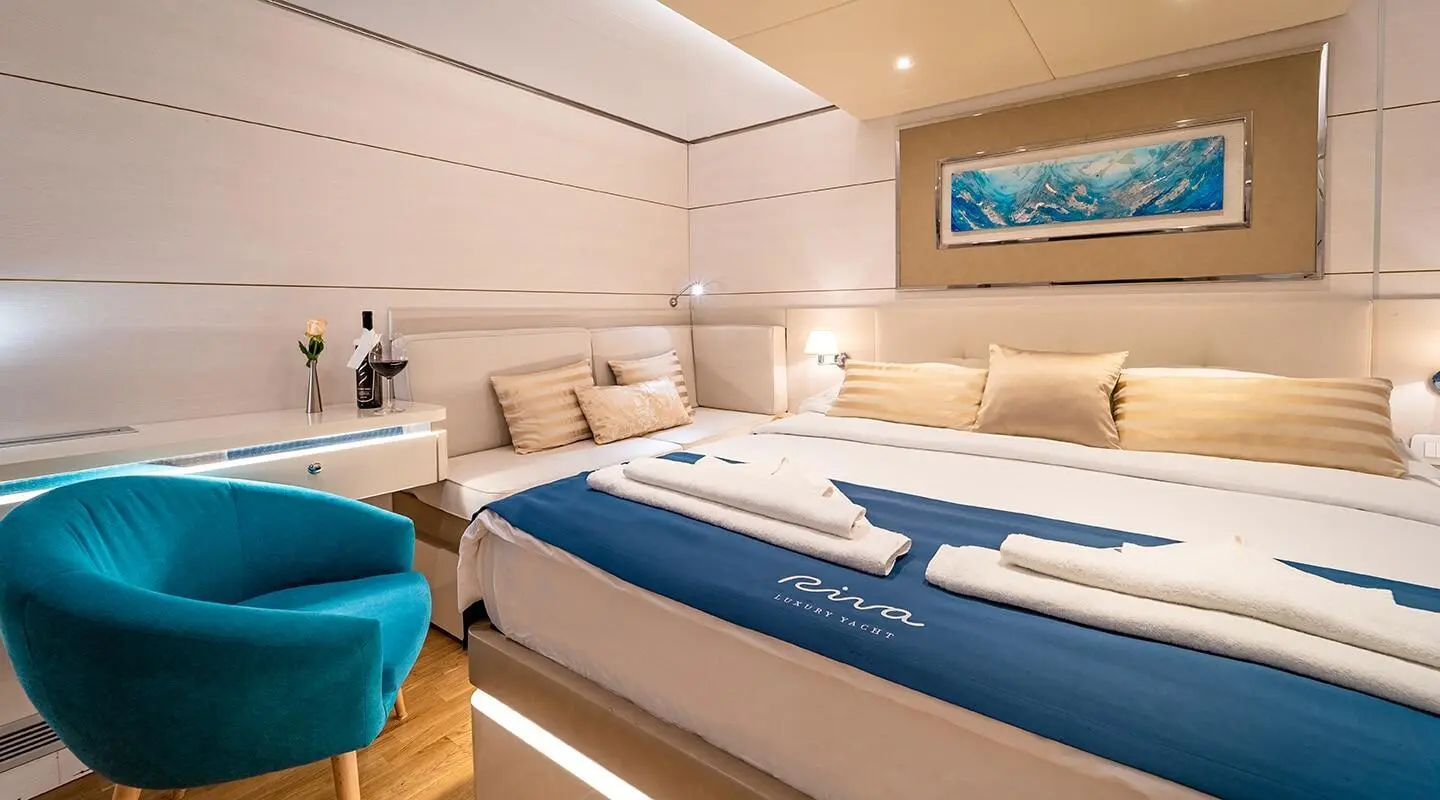 A luxury yacht bedroom with two large beds, white and blue bedding, built-in drawers, and soft lighting