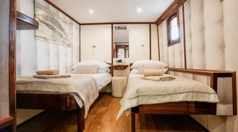 Luxurious yacht Mendula cabin interior with two beds, wood floor, and large window views