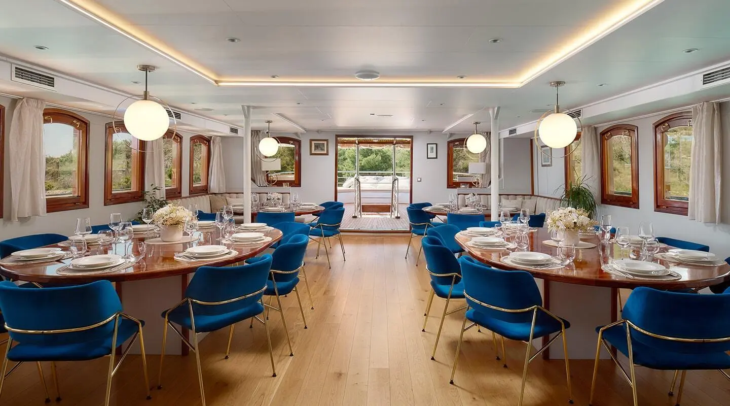 Inside the Bellezza yacht with round wooden tables set for dining and blue chairs.