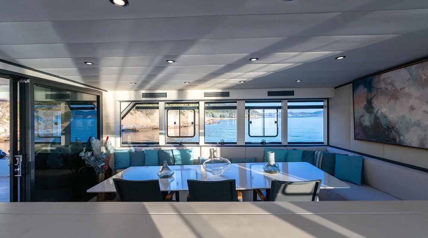 Calm Down yacht salon: blue cushioned seating along windows with a glass table