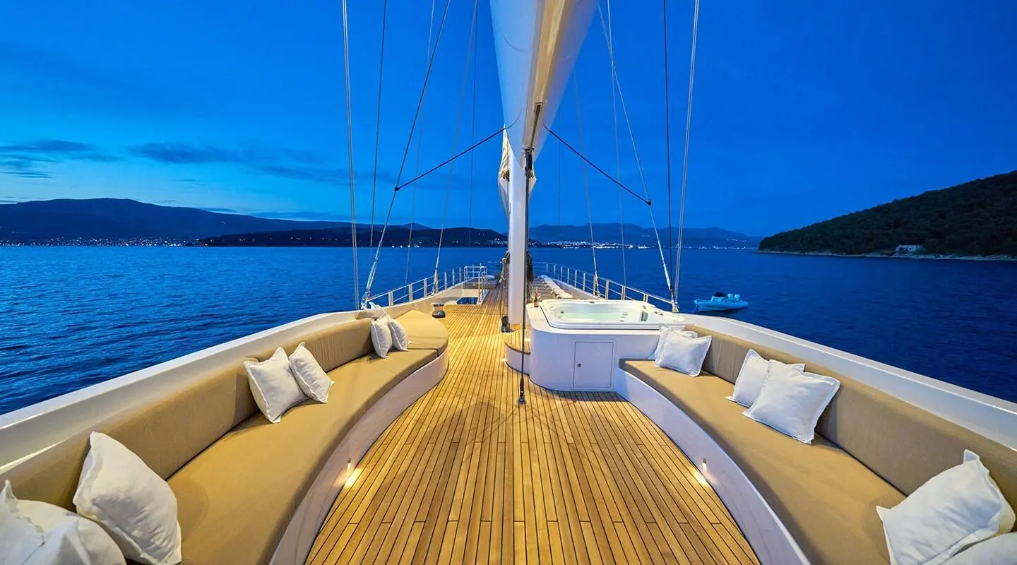 Sunlit deck of Acapella yacht with wood planks and seating under blue sky