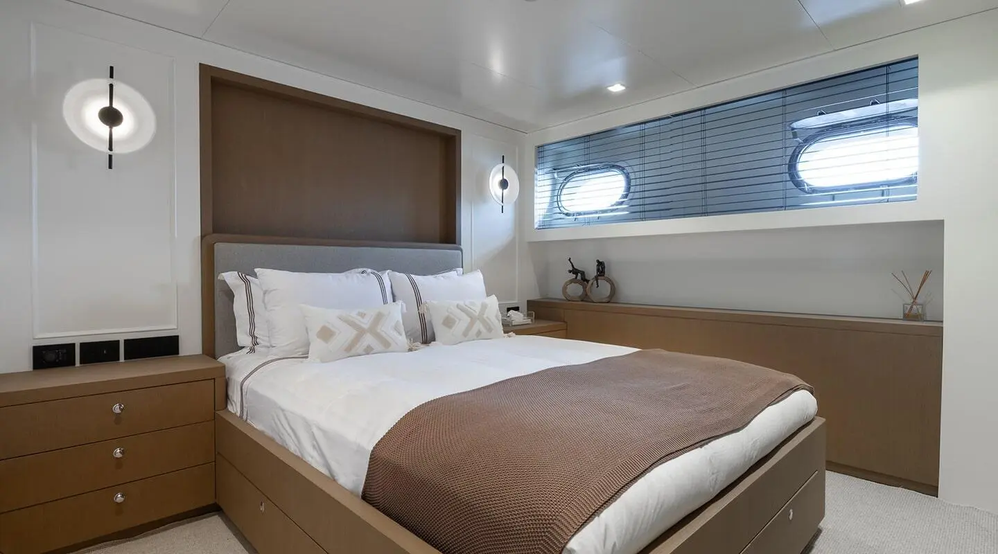 Interior of a yacht cabin with a large bed, wooden drawers and decorative items